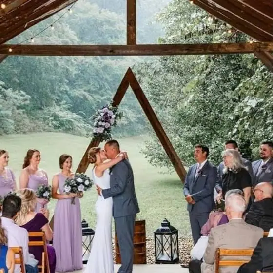A bride and groom sharing their first kiss under a triangular wooden arch in the covered pavilion